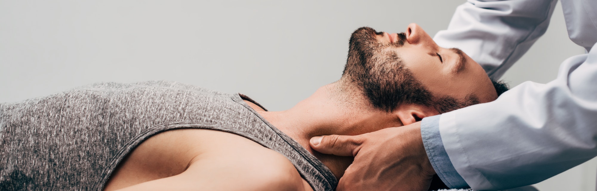 panoramic shot of chiropractor massaging neck of man on grey